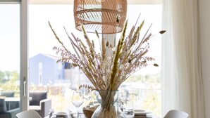 A dining table with a vase of dried plants, clear glasses, and a woven light fixture. - Harbour appartment with private garden (Kortgene)