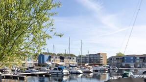 A marina with boats docked, a waterfront building, and a tree in the foreground. - Harbour appartment with private garden (Kortgene)