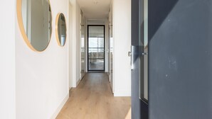Un pasillo con dos espejos redondos en la pared, una puerta oscura y vista a una habitación con cama y ventana.