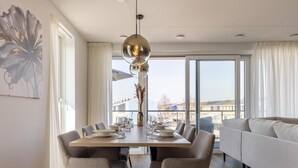 Un comedor moderno con una mesa de madera, seis sillas, una lámpara colgante grande y vistas de la ciudad a través de amplios ventanales.