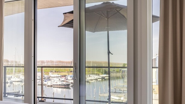 Habitación de hotel con un amplio ventanal que da a un puerto deportivo con barcos.