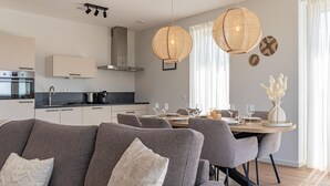 A modern living room with a sofa, dining table, and chairs. There is a kitchen area with appliances and cabinets. - Luxury penthouse with terrace and harbour views (Kortgene)