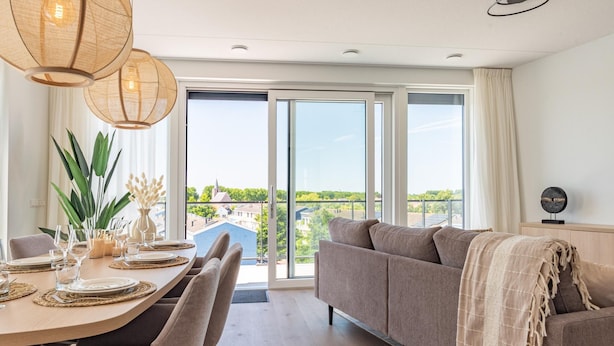 A modern living room with a dining area, large windows, and a view of the cityscape. - Luxury penthouse with terrace and harbour views (Kortgene)