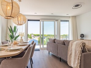 A modern living room with a dining area, large windows, and a view of the cityscape. - Luxury penthouse with terrace and harbour views (Kortgene)