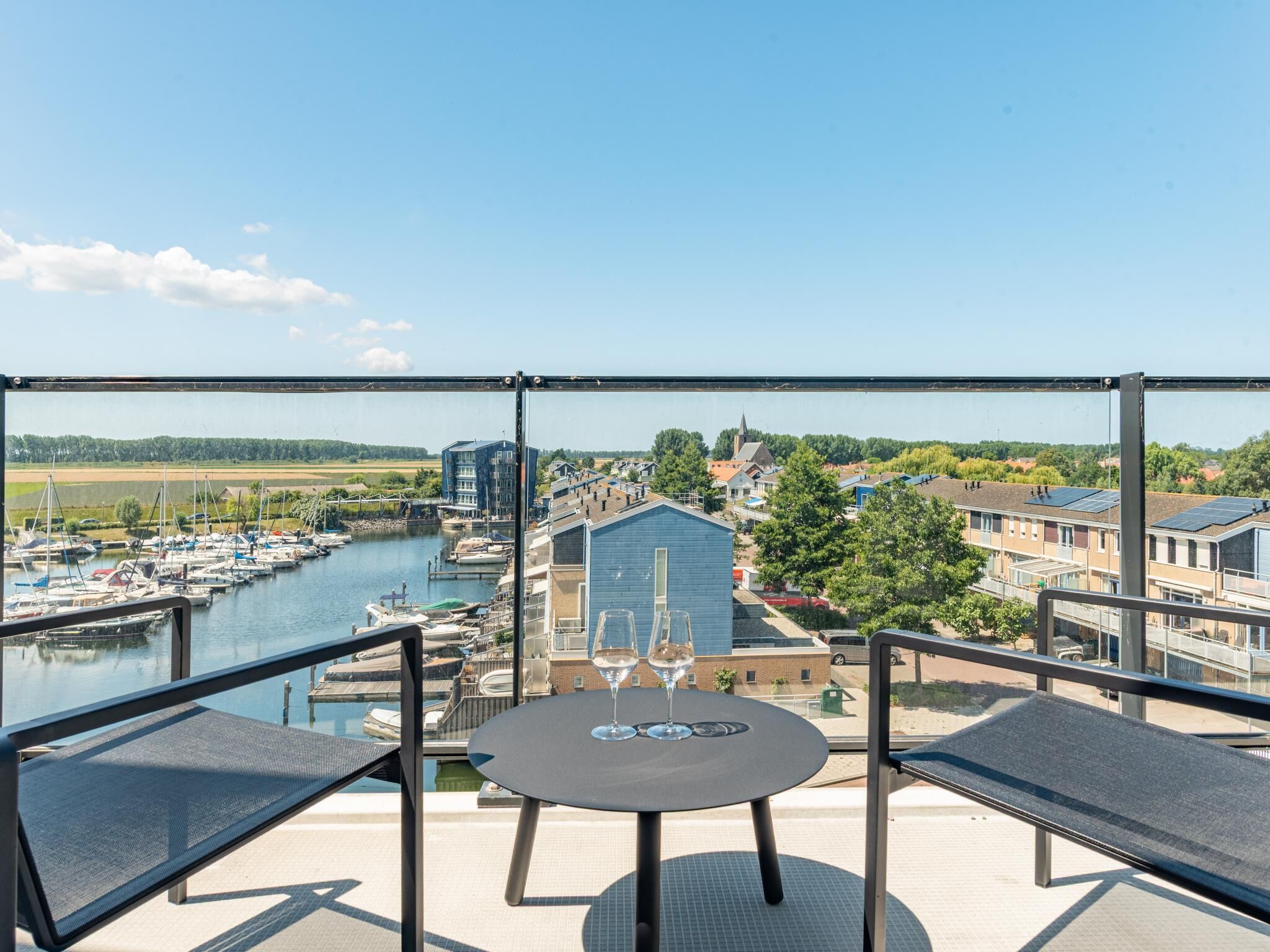 Un balcon avec une table et des chaises donnant sur une marina où l’on peut admirer des bateaux et des bâtiments.