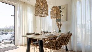 Zona pranzo con tavolo apparecchiato per quattro, sedie in vimini e due lampade pendenti in vimini.