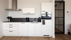 Una cucina moderna con mobili bianchi, un piano di lavoro nero, una macchina per il caffè e una cappa aspirante in acciaio inossidabile.