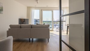 Un soggiorno moderno con divano, televisore e vista di una marina attraverso ampie finestre.