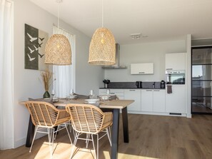 A modern kitchen with white cabinets, a dining table with chairs, and hanging wicker light fixtures. - Harbour apartment with beautiful views (Kortgene)