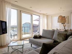 A modern living room with a sofa, a glass coffee table, and a TV mounted on the wall. - Harbour apartment with beautiful views (Kortgene)
