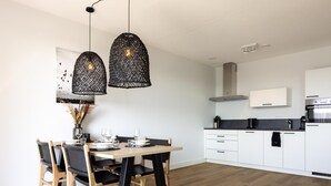 Une cuisine moderne avec des meubles blancs, un plan de travail noir et un coin repas comprenant une table et des chaises en bois.