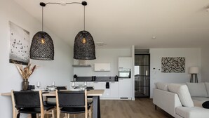 Une cuisine moderne avec des meubles blancs, un coin repas doté d’une table et de chaises en bois, et un salon avec un canapé.