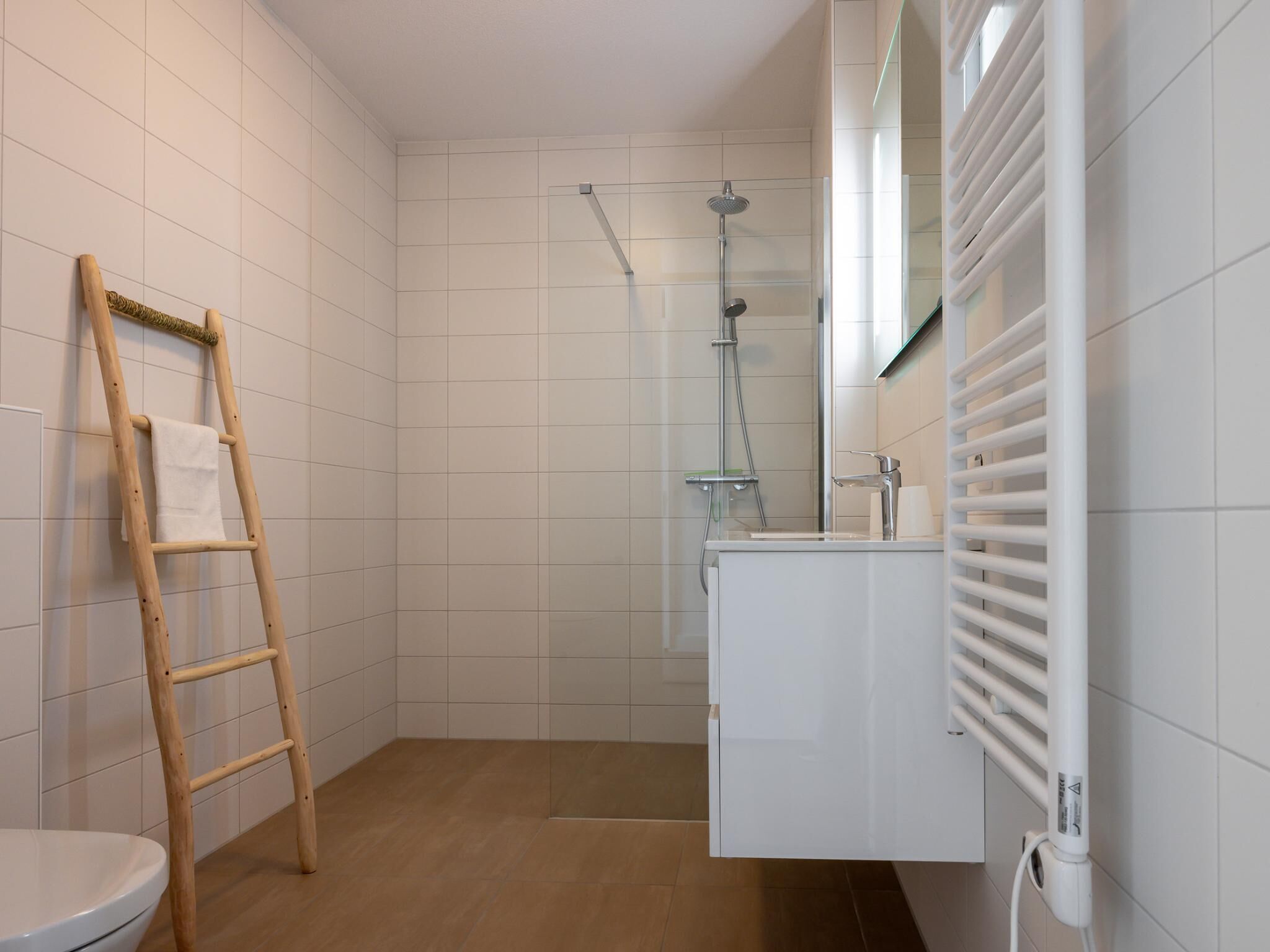 Ein Badezimmer mit einer Holzleiter, einer Dusche, einer Toilette und einem Waschbecken mit Spiegel.