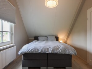 A bedroom with a sloped ceiling, a bed with a striped bedspread, a window with blinds, and a radiator. - Villa with private pool on the Eastern Scheldt (Wissenkerke)