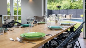 A dining area with a long table set for a meal, surrounded by chairs, with a view of a backyard and a swimming pool. - Villa with private pool on the Eastern Scheldt (Wissenkerke)