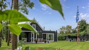 A house with a large lawn, a flag, and a tree in the foreground. - Villa with private pool on the Eastern Scheldt (Wissenkerke)