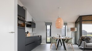 Ett modernt kök med mörka skåp, en matplats med ett runt bord och stolar samt ett stort fönster med fin utsikt.