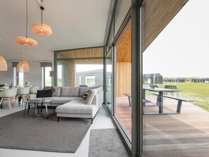 Un interno moderno con un'ampia vetrata che si apre su una terrazza esterna, un divano angolare grigio e un'area pranzo con tavolo e sedie.