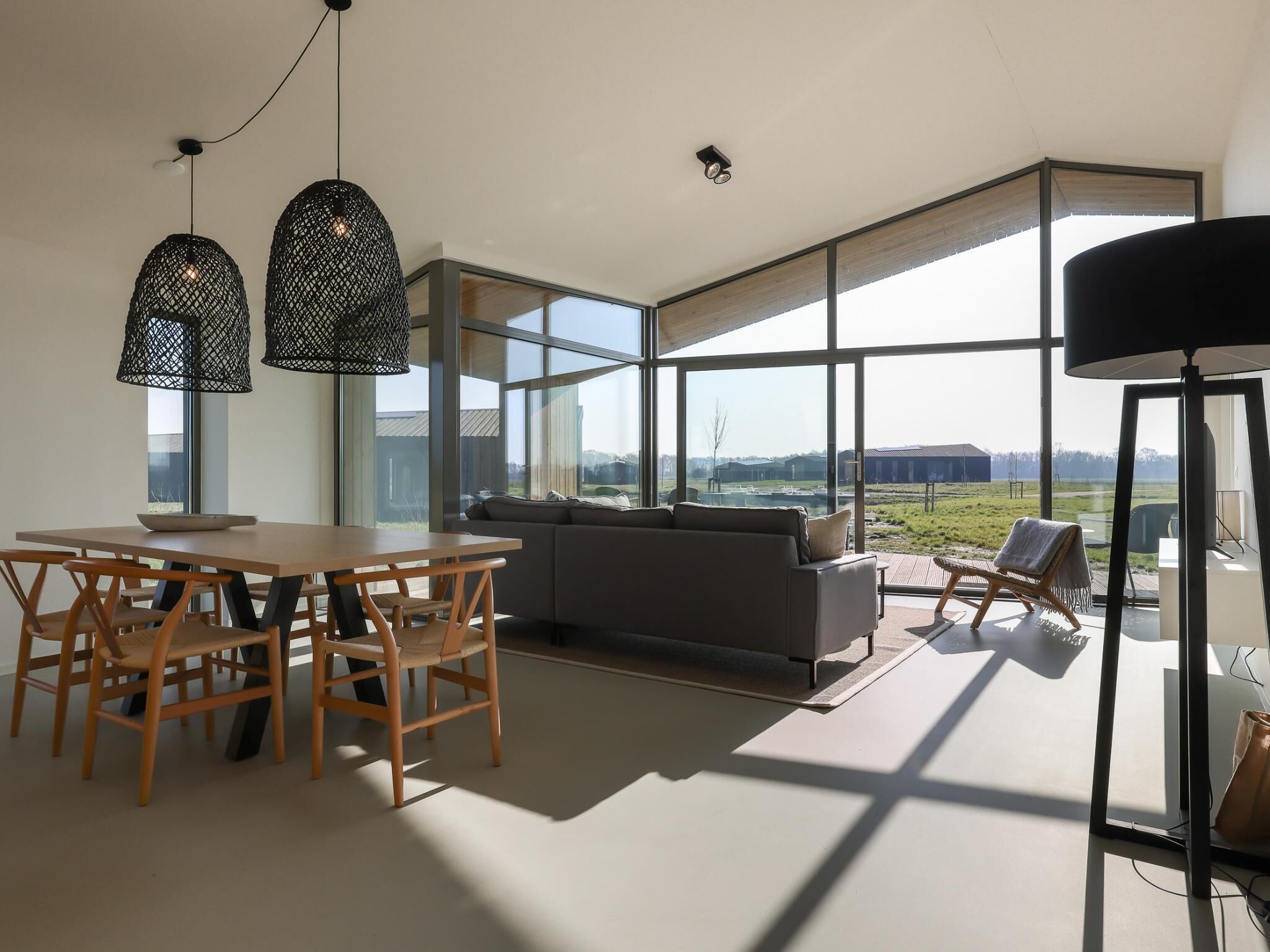 A modern interior with a dining area, sofa, and large windows offering a view of the outdoors.