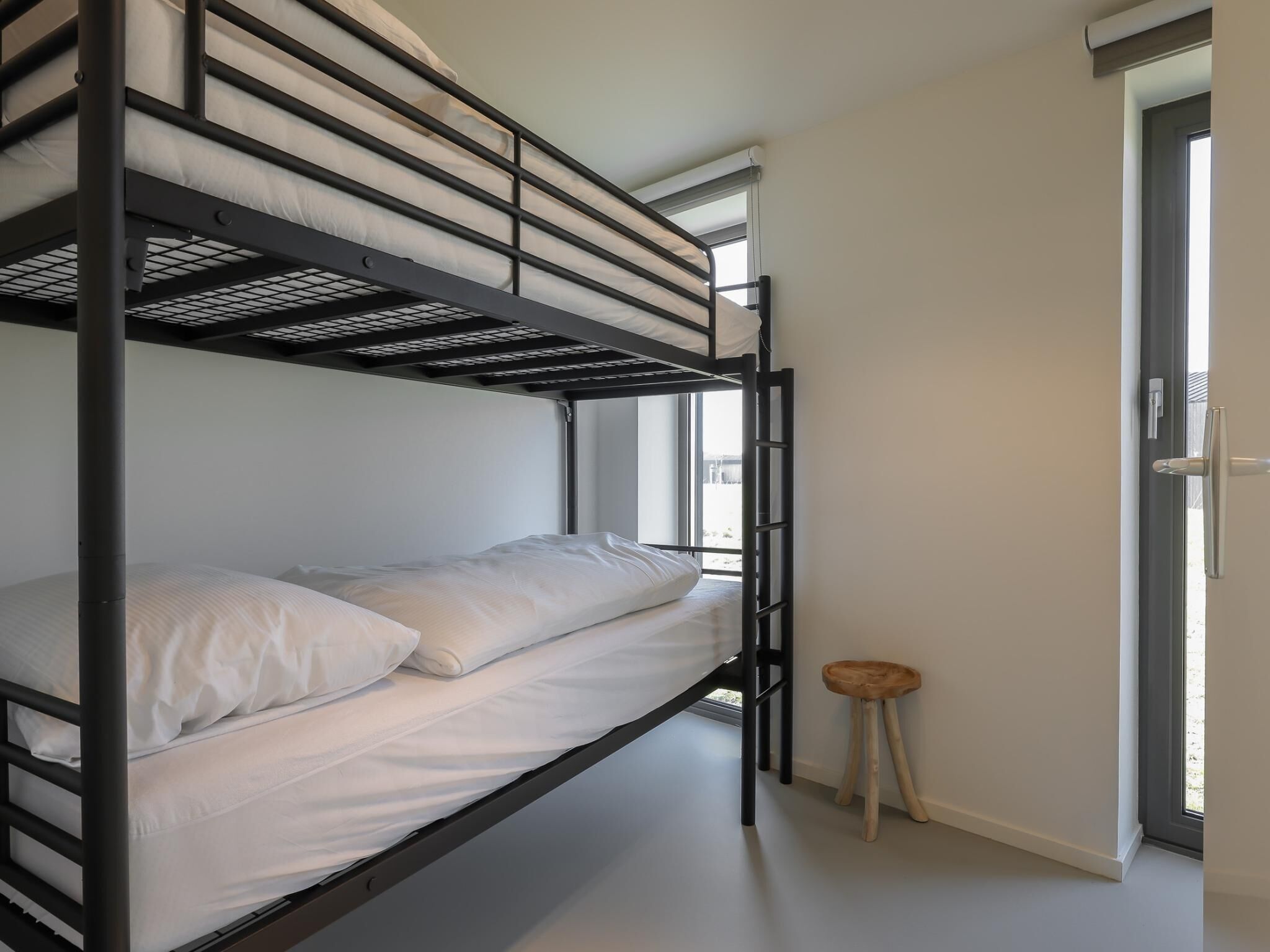 A bunk bed with a ladder, a small stool, and a door leading outside.