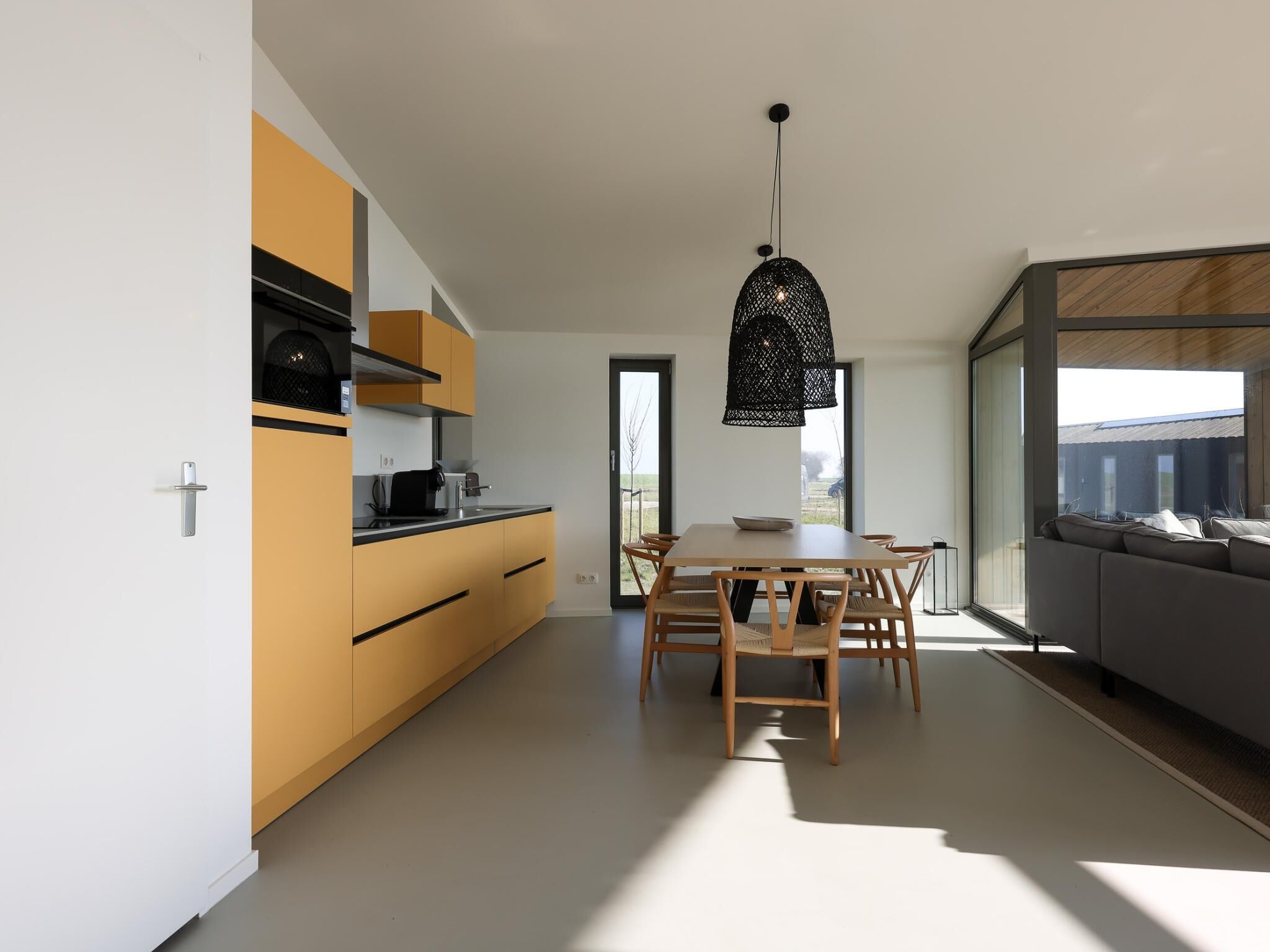A modern kitchen with a dining area, a black pendant light, and a view of the outdoors.