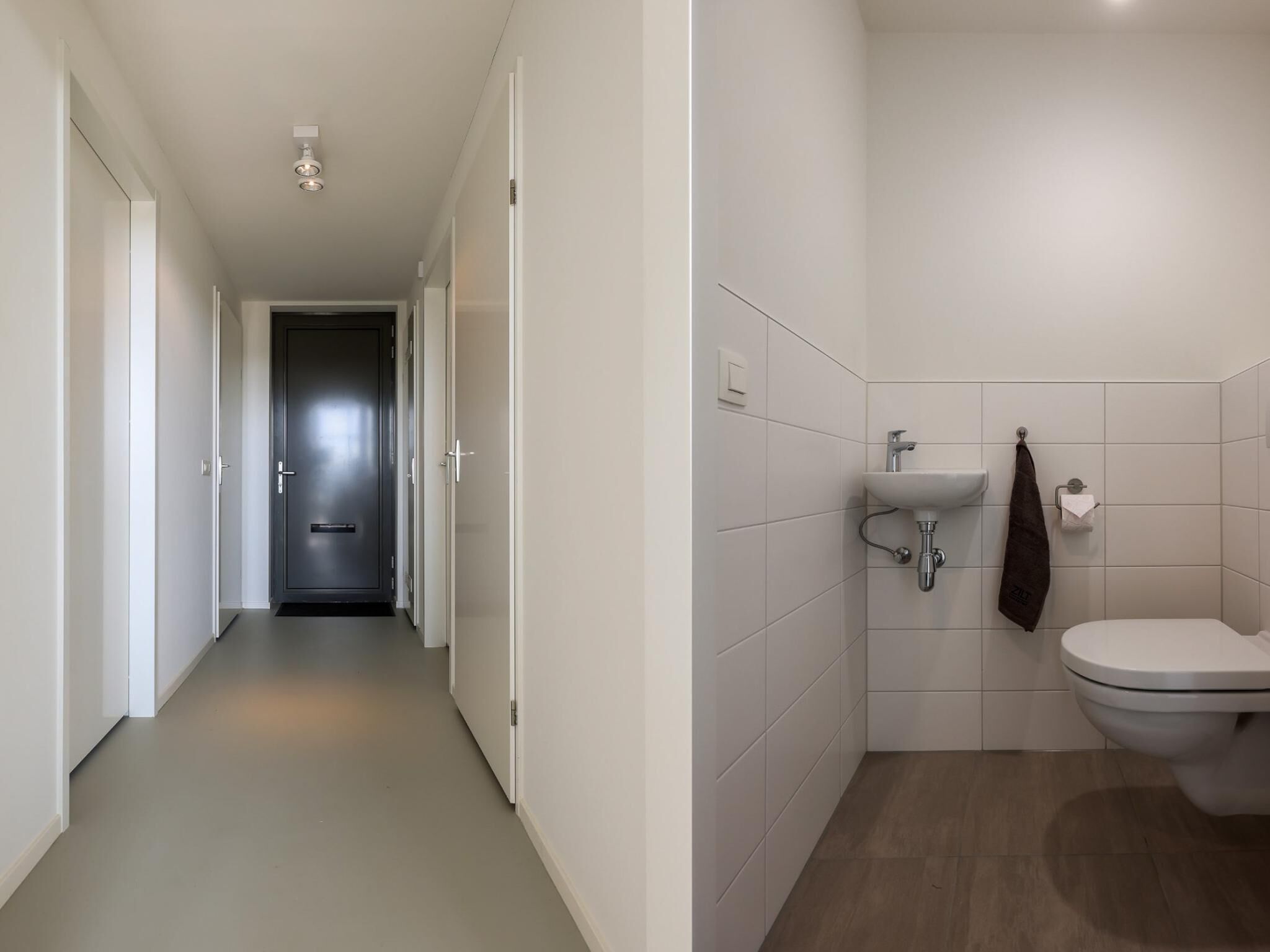 A hallway leading to a door, a bathroom with a sink, toilet, and towel rack.