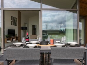 A dining table set with plates, glasses, and a bottle of wine, with a view of the outdoors through large windows. - Holiday home with terrace and wide views (Wissenkerke)