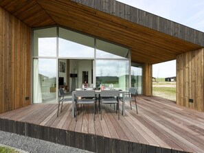 A modern building with a wooden deck, large glass windows, and a dining area with tables and chairs. - Holiday home with terrace and wide views (Wissenkerke)