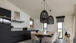 Una cocina moderna con armarios oscuros, una mesa de comedor de madera y luces colgantes.