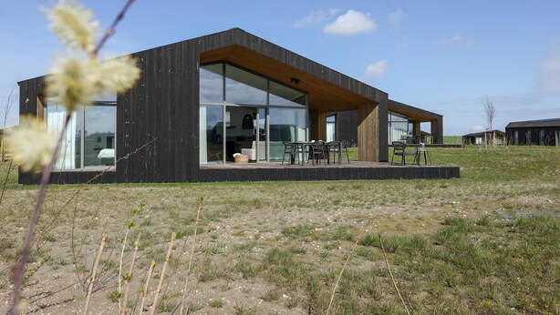 Una casa moderna con amplios ventanales, una terraza de madera y un jardín césped.