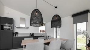 Una cocina moderna con zona de comedor, que incluye una mesa de madera, sillas grises y lámparas colgantes negras.