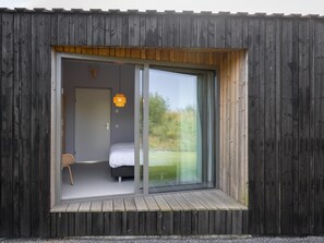 A modern room with a bed, a chair, and a large sliding glass door leading to an outdoor area. - Nature house with views over fields (Wissenkerke)