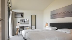 Ein modernes Schlafzimmer mit einem großen Bett, einem Schreibtisch, einem Stuhl, einem Spiegel und Kunstwerken an den Wänden.