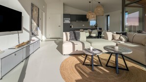 A modern living room with a flat-screen TV, a sofa, a coffee table, and a dining area with a kitchen in the background. - Nature house with 2 bathrooms (Wissenkerke)