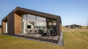 A modern house with a large glass window, a wooden deck, and a dining area with chairs. - Nature house with 2 bathrooms (Wissenkerke)