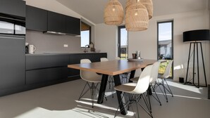 A modern kitchen with dark cabinets, a wooden dining table, and white chairs. - Nature house with 2 bathrooms (Wissenkerke)