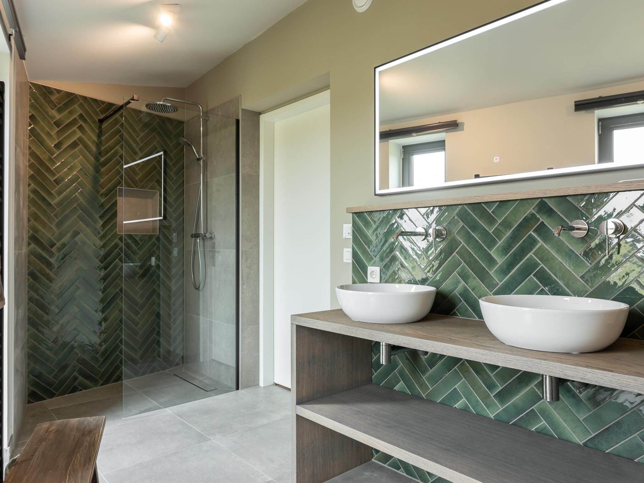 A modern bathroom with a glass shower enclosure, two vessel sinks, and a herringbone tile backsplash.