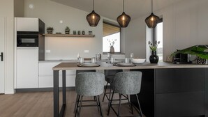 A modern kitchen with a central island, bar stools, pendant lighting, and a built-in oven. - Nature house with sauna by nature reserve (Wissenkerke)
