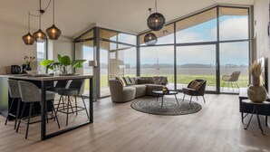 A modern interior with a dining area, seating, and large windows offering a view of the outdoors. - Nature house with sauna by nature reserve (Wissenkerke)