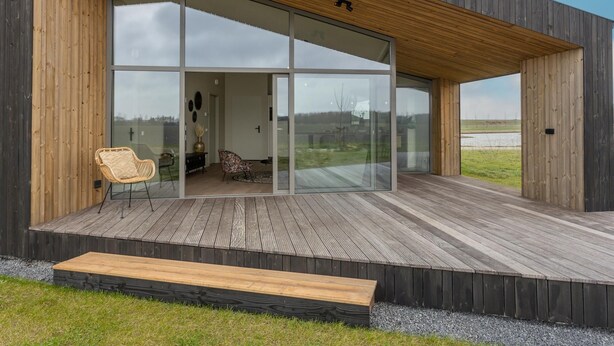 A modern house with a wooden deck, large glass doors, and a bench. - Nature house with sauna by nature reserve (Wissenkerke)