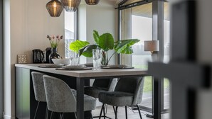 A modern dining area with a large table, three chairs, pendant lights, and a large plant. - Nature house with sauna by nature reserve (Wissenkerke)