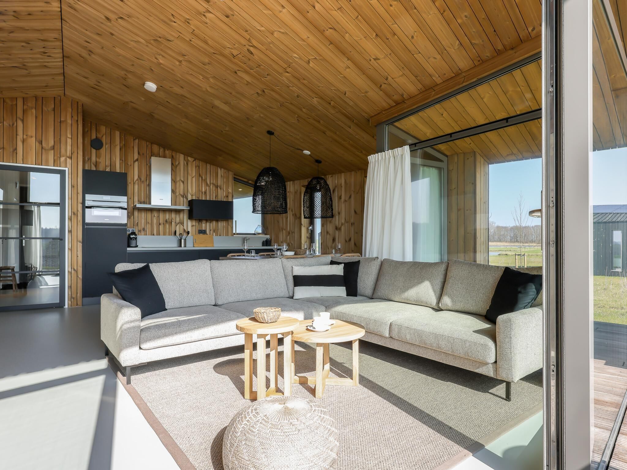 Een modern interieur met een houten plafond, een bank, een klein rond tafeltje en een keukenhoek.