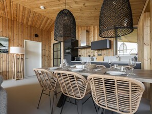 Een houten interieur met een eethoek, rieten stoelen, een tafel gedekt voor vier personen en hanglampen.