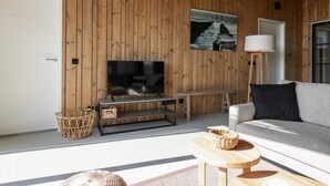 Un saló modern amb un panell de paret de fusta, un televisor de pantalla plana, un sofà, una làmpada de peu i una taula petita.