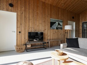 Ein modernes Wohnzimmer mit Holzpaneelen, einem Flachbildfernseher, einer Couch, einer Stehlampe und einem kleinen Tisch.