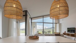 Et moderne spiseområde med et stort bord, hvide stole og to store vævede lysekroner.