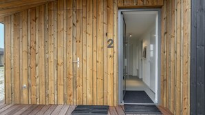 En facade i træ med en dør markeret '2', et metalgreb og en sort dørmåtte ved indgangen.