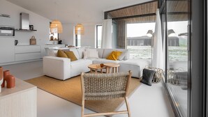 En moderne stue med sofa, lænestol, lille bord og et køkkenområde med mikroovn.