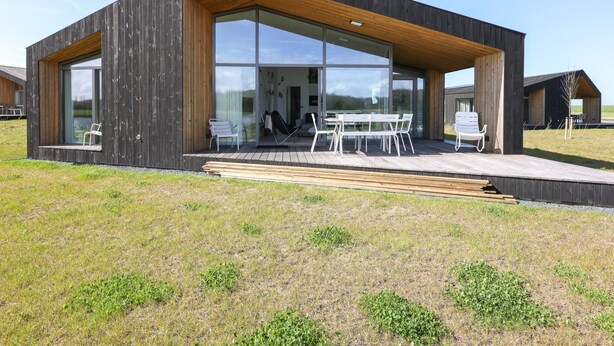 A modern house with large glass windows, a wooden deck, and outdoor seating. - Beautiful nature house with terrace by the water (Wissenkerke)