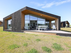 Una casa moderna con amplios ventanales, una terraza de madera y mobiliario exterior.
